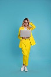 Young woman with modern laptop on light blue background