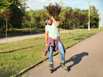 Photo of Handsome young man roller skating in park, space for text