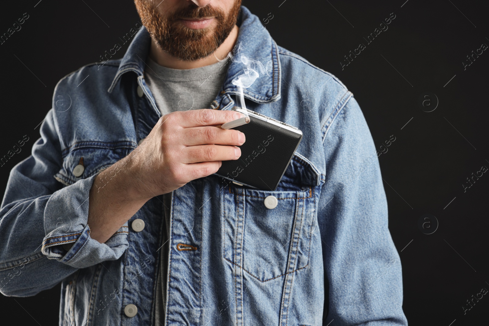 Photo of Man putting cigarette case into pocket on black background, closeup