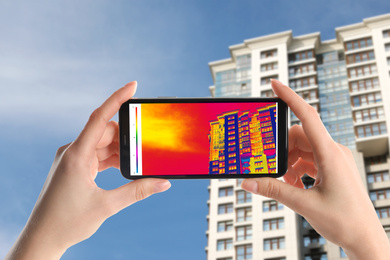 Image of Woman detecting heat loss in building using thermal viewer on smartphone, outdoors. Energy efficiency