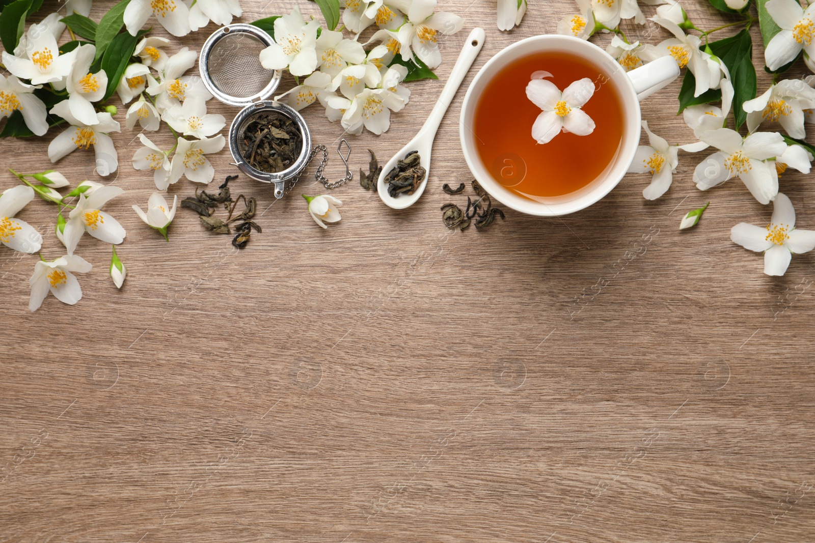 Photo of Cup of aromatic jasmine tea and fresh flowers on wooden table, flat lay. Space for text