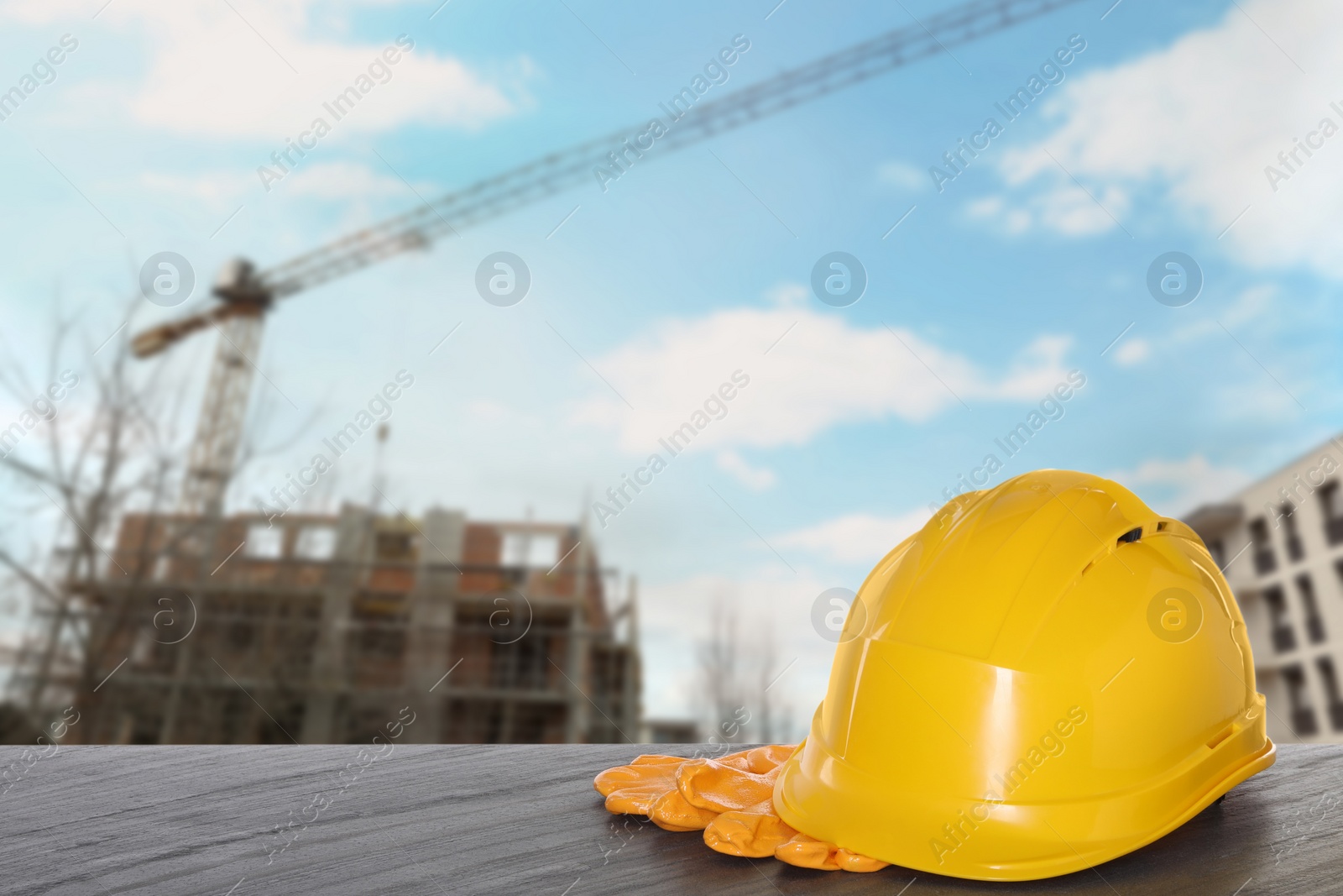 Image of Safety equipment. Hard hat and gloves on wooden surface near unfinished building outdoors, space for text