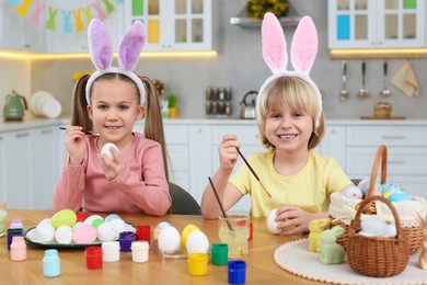Children painting Easter eggs at table in kitchen
