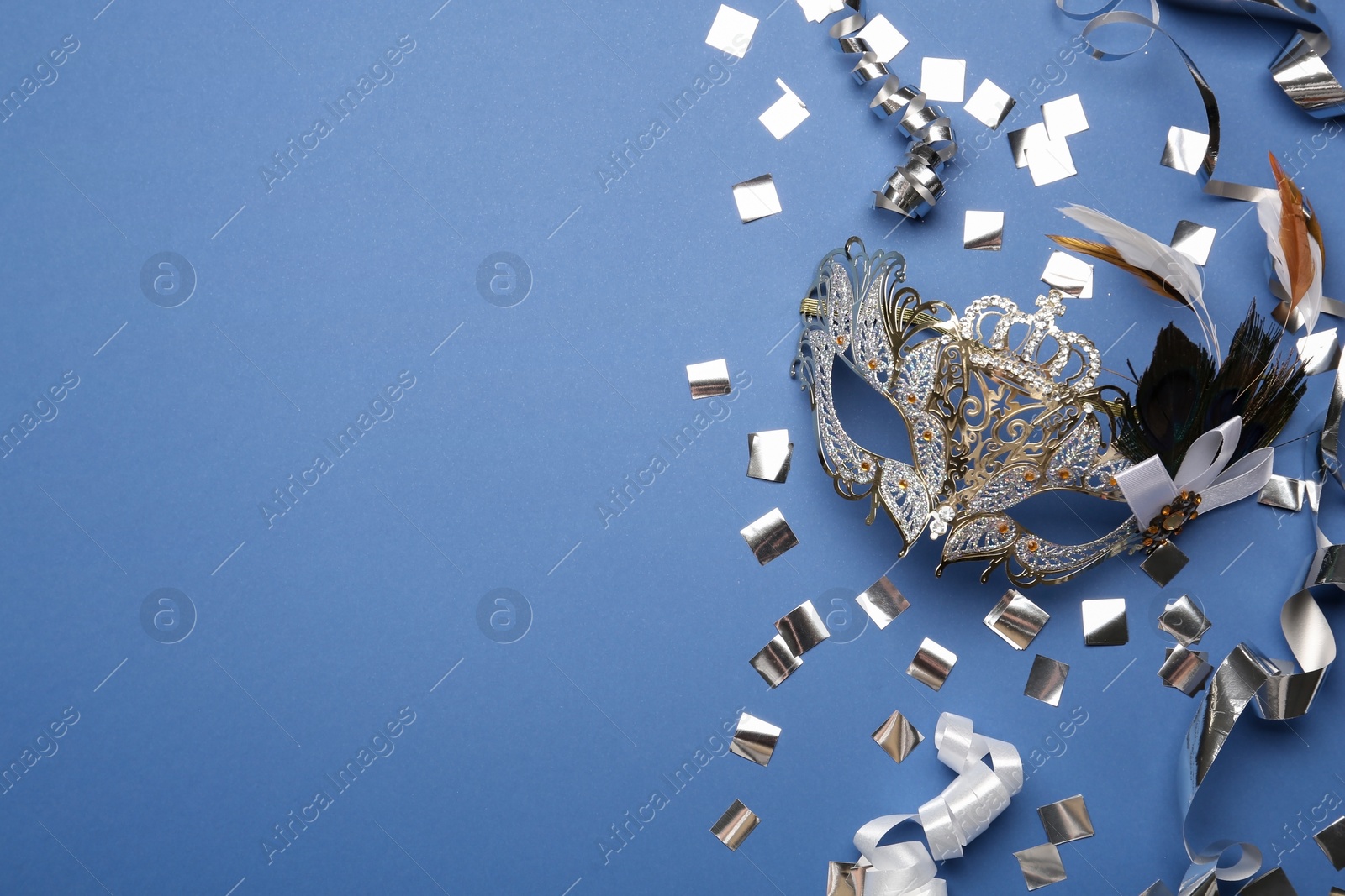 Photo of Beautiful carnival mask and shiny confetti on blue background, flat lay. Space for text