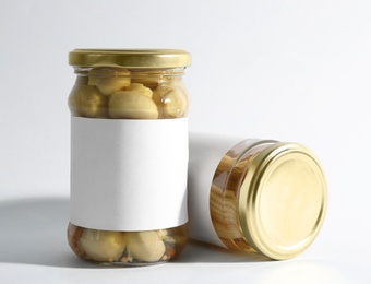 Photo of Glass jars with pickled mushrooms and baby corn on white background
