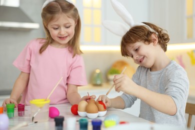 Easter celebration. Cute children with bunny ears painting eggs at white marble table in kitchen