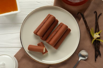 Photo of Glazed curd cheese bars, vanilla pods and flower on white wooden table, flat lay