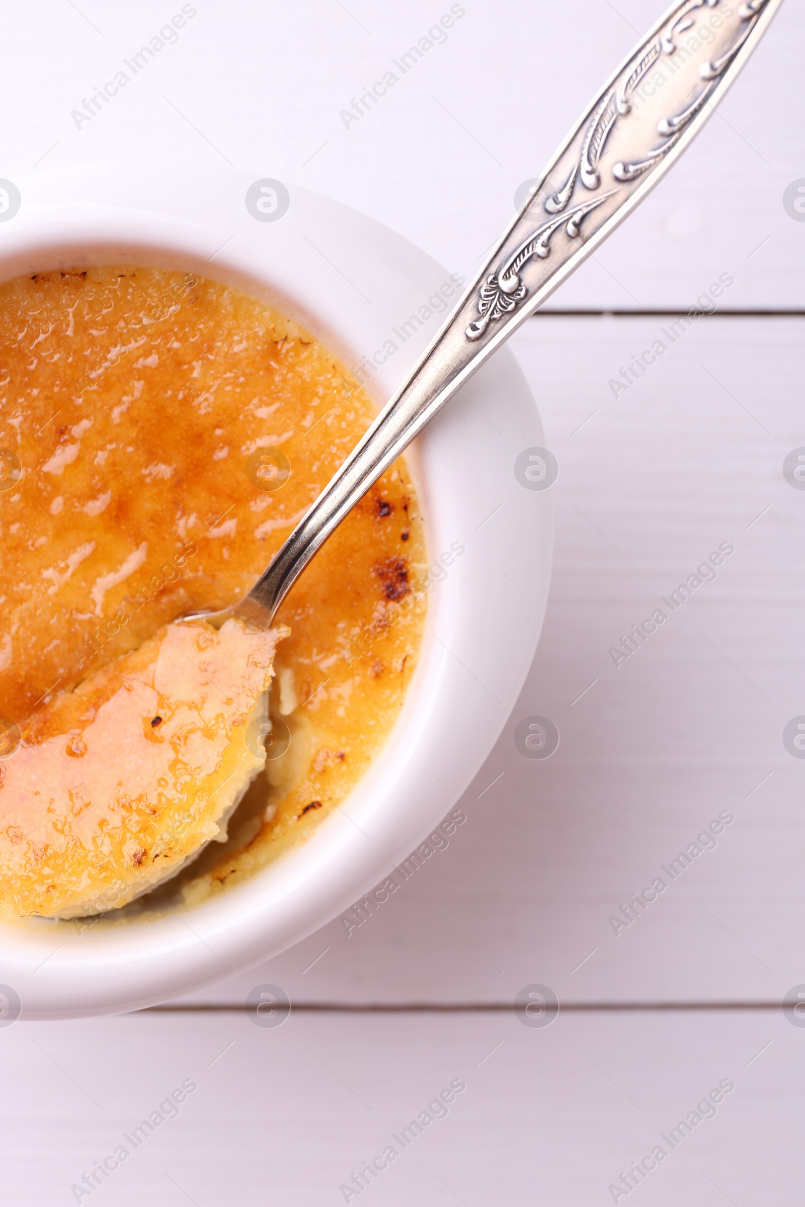 Photo of Delicious creme brulee in bowl served on white wooden table, top view