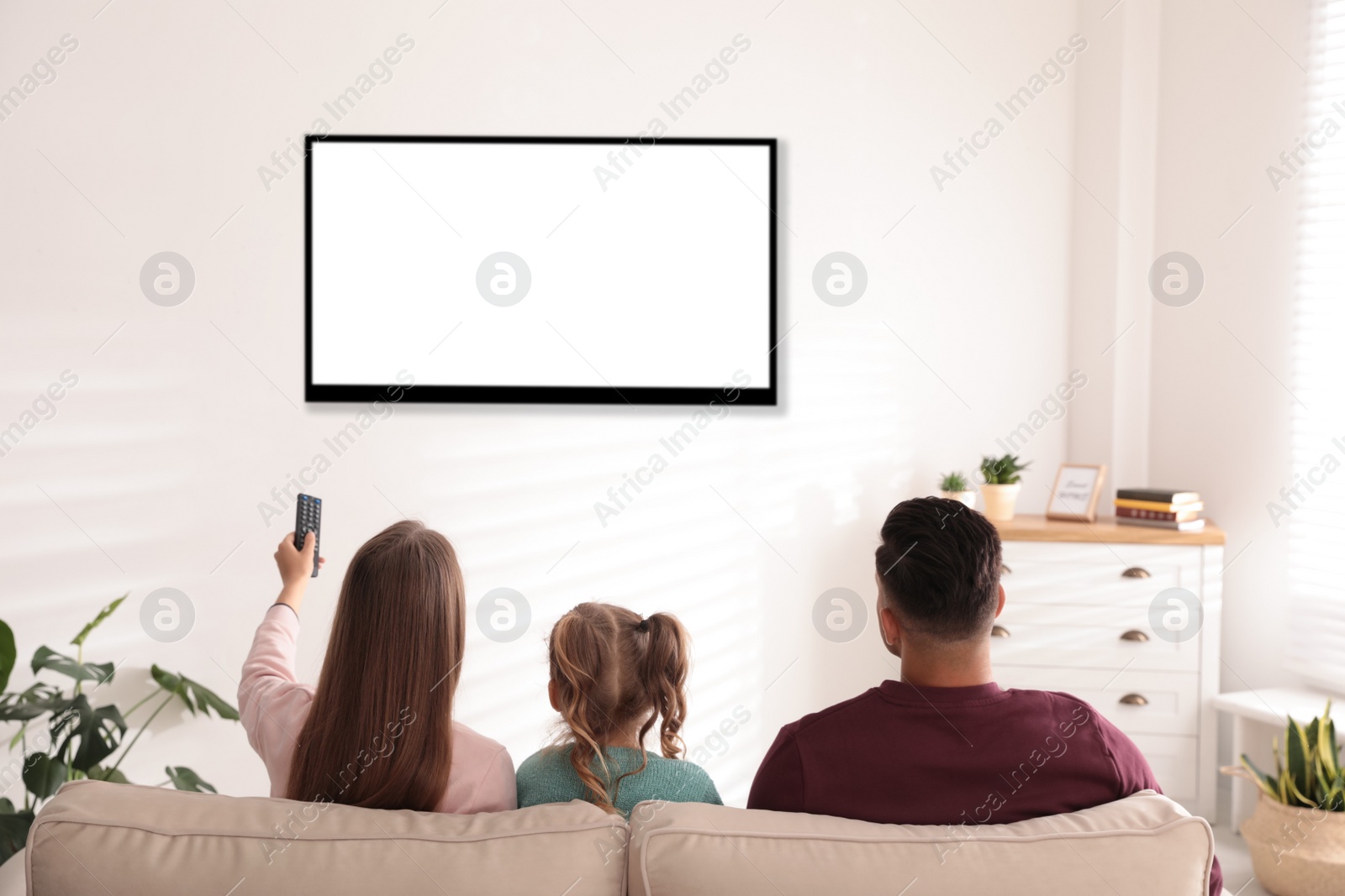 Photo of Family watching TV on sofa at home, back view