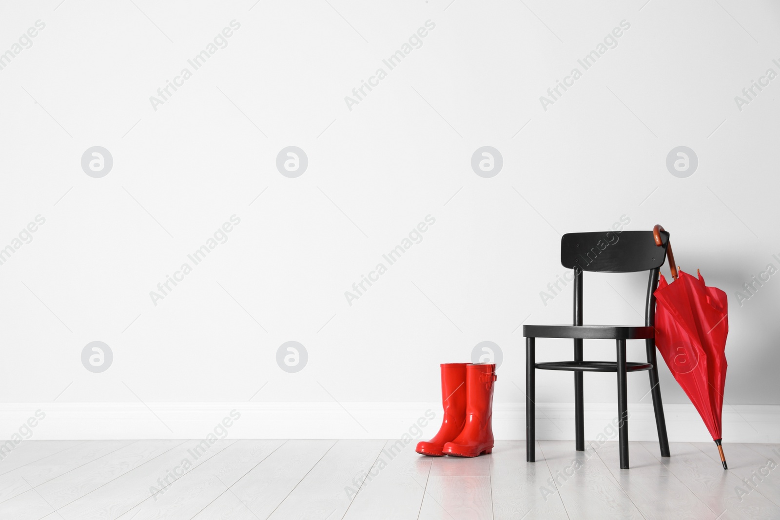 Photo of Umbrella, gumboots and chair on floor near white wall with space for design