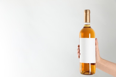 Woman holding bottle of white wine on light background, closeup. Space for text