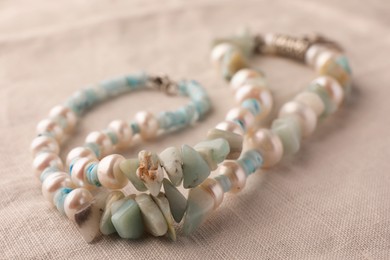 Photo of Beautiful necklace with gemstones on light cloth, closeup