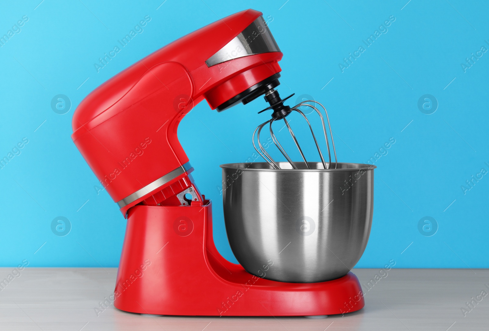 Photo of Modern red stand mixer on white wooden table against turquoise background