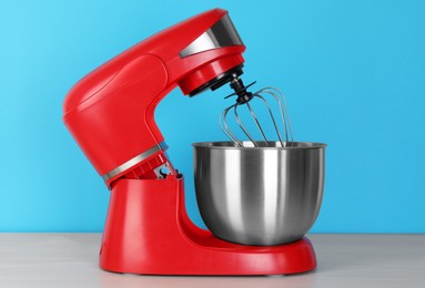 Photo of Modern red stand mixer on white wooden table against turquoise background