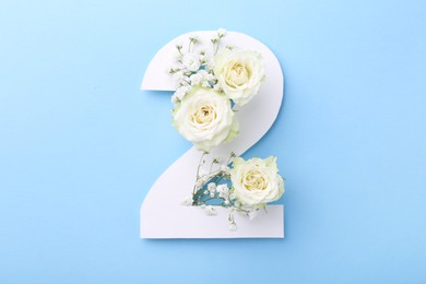 Photo of Paper number 2 and beautiful flowers on light blue background, top view