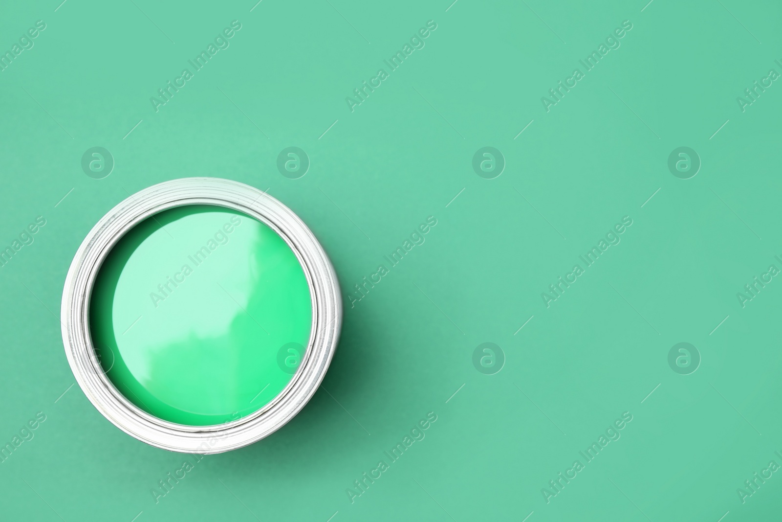 Photo of Open can of paint on green background, top view. Space for text