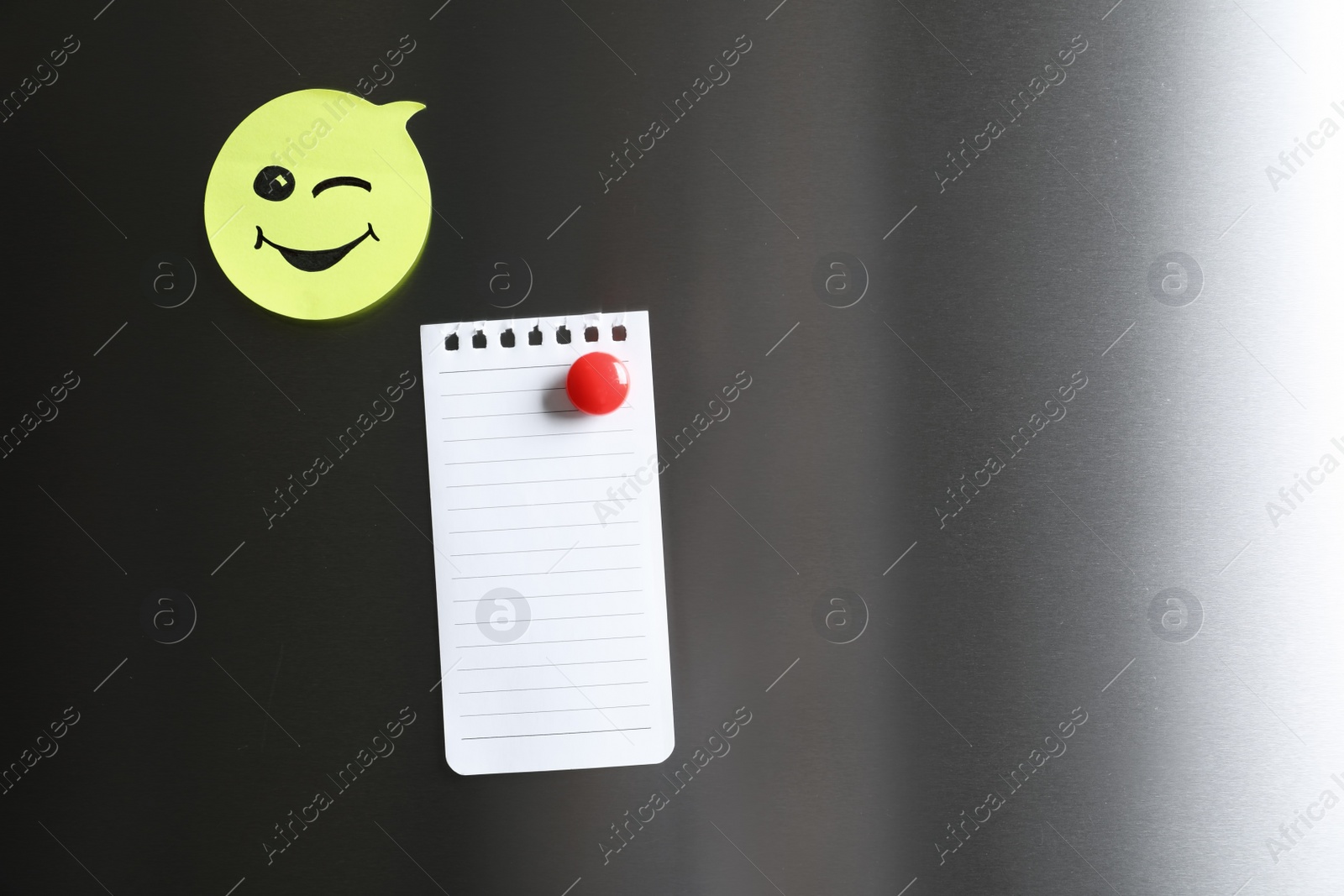 Photo of Blank note and sticker with funny face on refrigerator door. Space for text