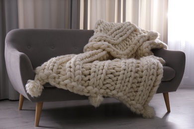 Photo of Soft knitted blanket on couch in living room. Interior element