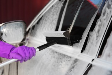 Photo of Worker cleaning automobile with squeegee at car wash, closeup