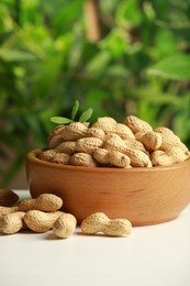 Photo of Fresh unpeeled peanuts in bowl on white table against blurred background