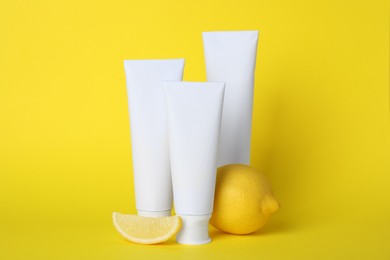 Photo of Blank tubes of toothpaste and fresh lemon on yellow background