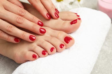 Photo of Woman showing stylish toenails after pedicure procedure and manicured hands with red polish on grey floor, closeup