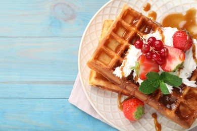 Photo of Delicious Belgian waffles with berries and caramel sauce served on turquoise wooden table, top view. Space for text