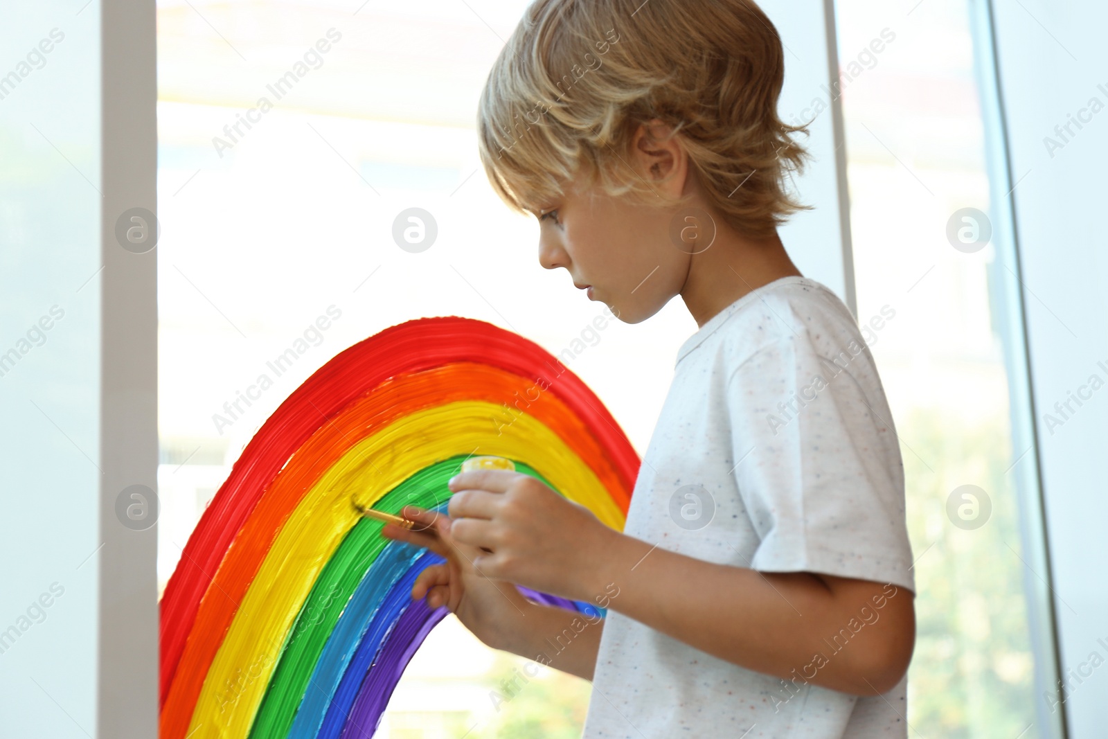 Photo of Little boy drawing rainbow on window. Stay at home concept