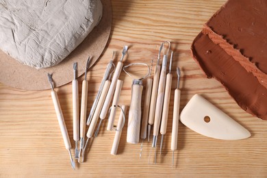 Photo of Clay and set of modeling tools on wooden table, flat lay