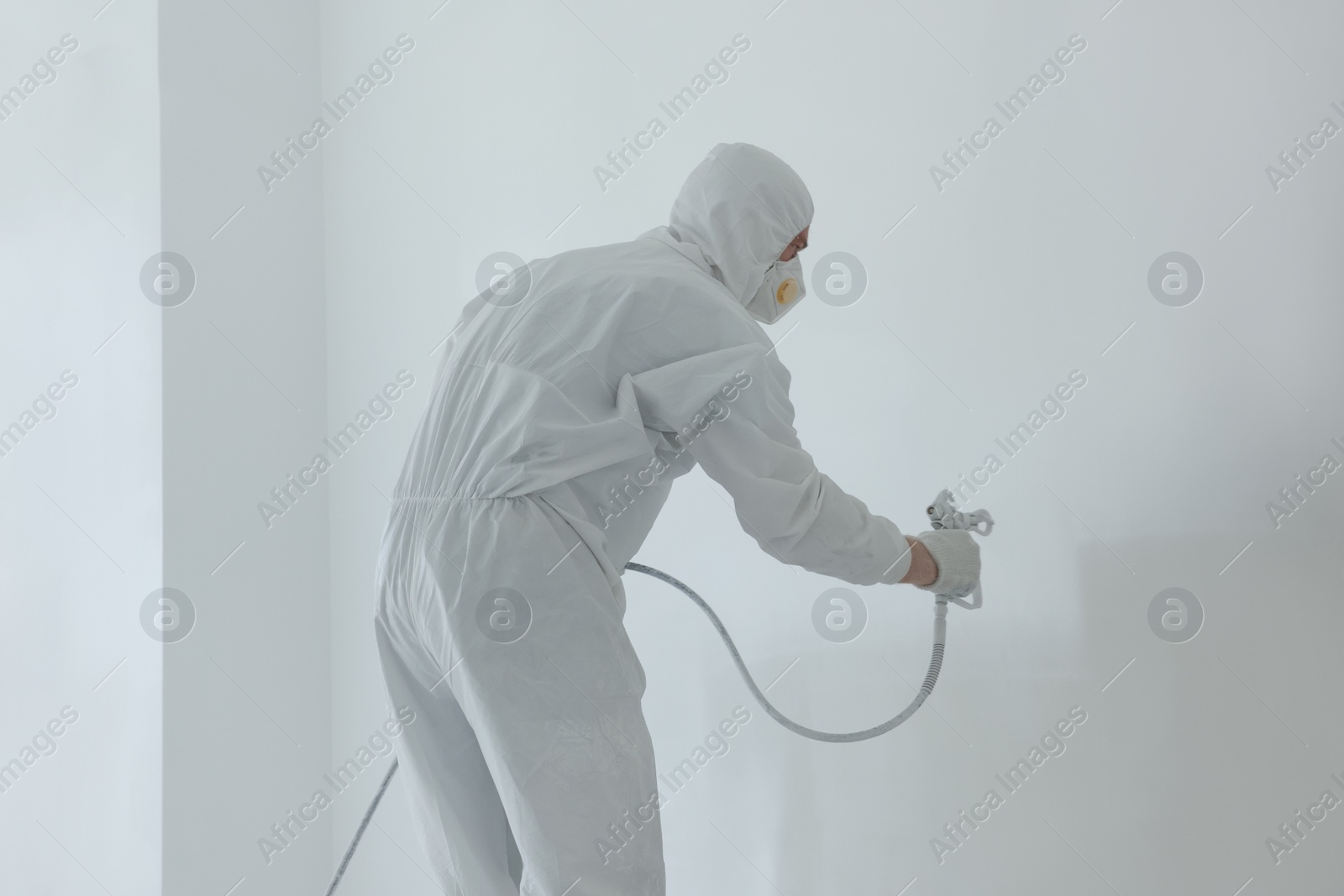 Photo of Decorator painting white wall with spray indoors