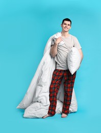 Photo of Happy man in pyjama holding blanket and pillow on light blue background