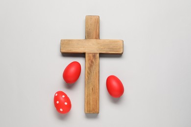 Wooden cross and painted Easter eggs on light grey background, flat lay