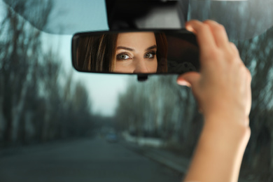 Young woman adjusting rear view mirror in car, closeup