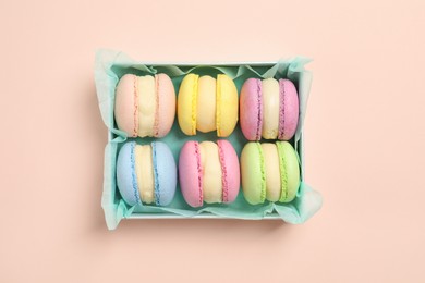 Many delicious colorful macarons in box on pink background, top view