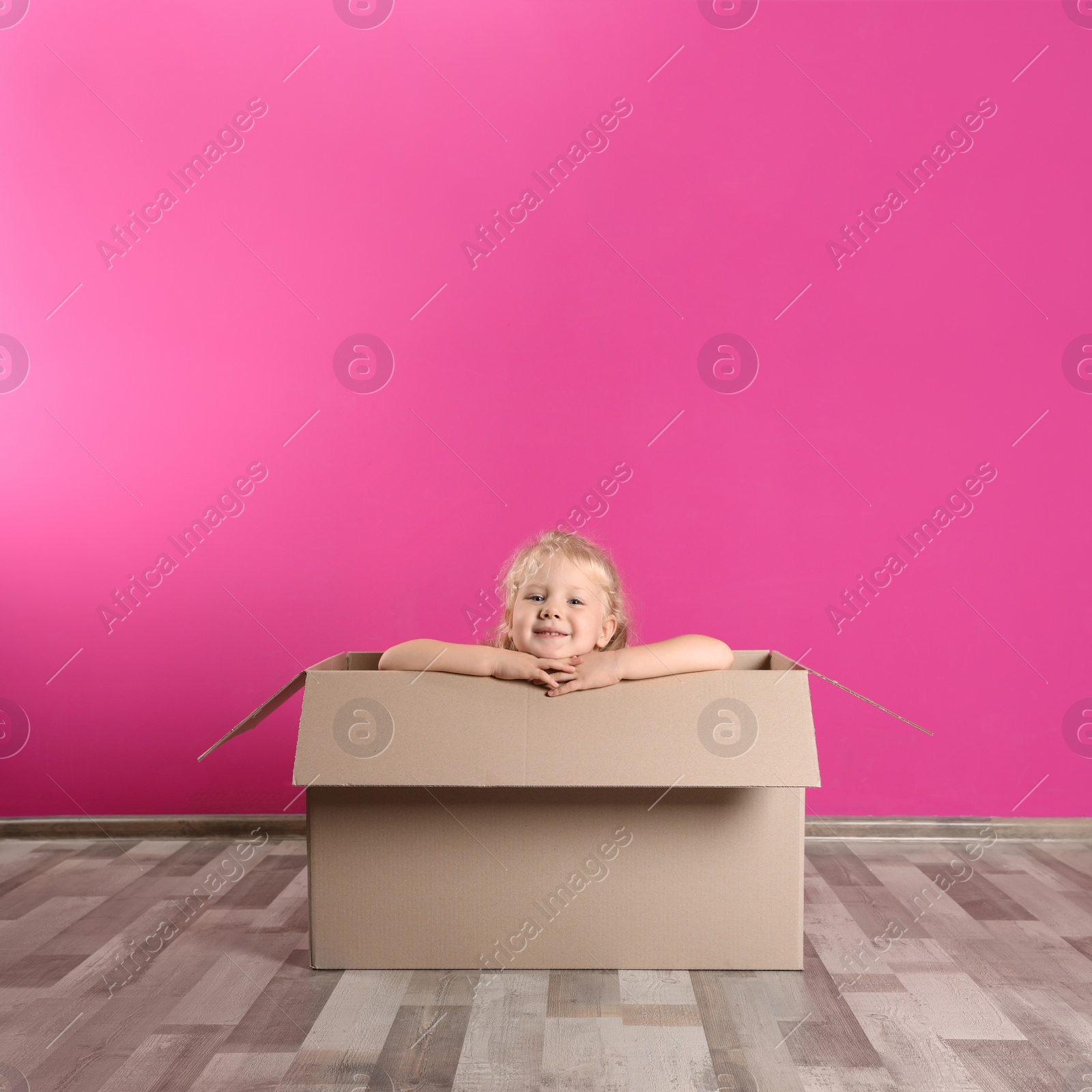 Photo of Cute little girl playing with cardboard box near color wall