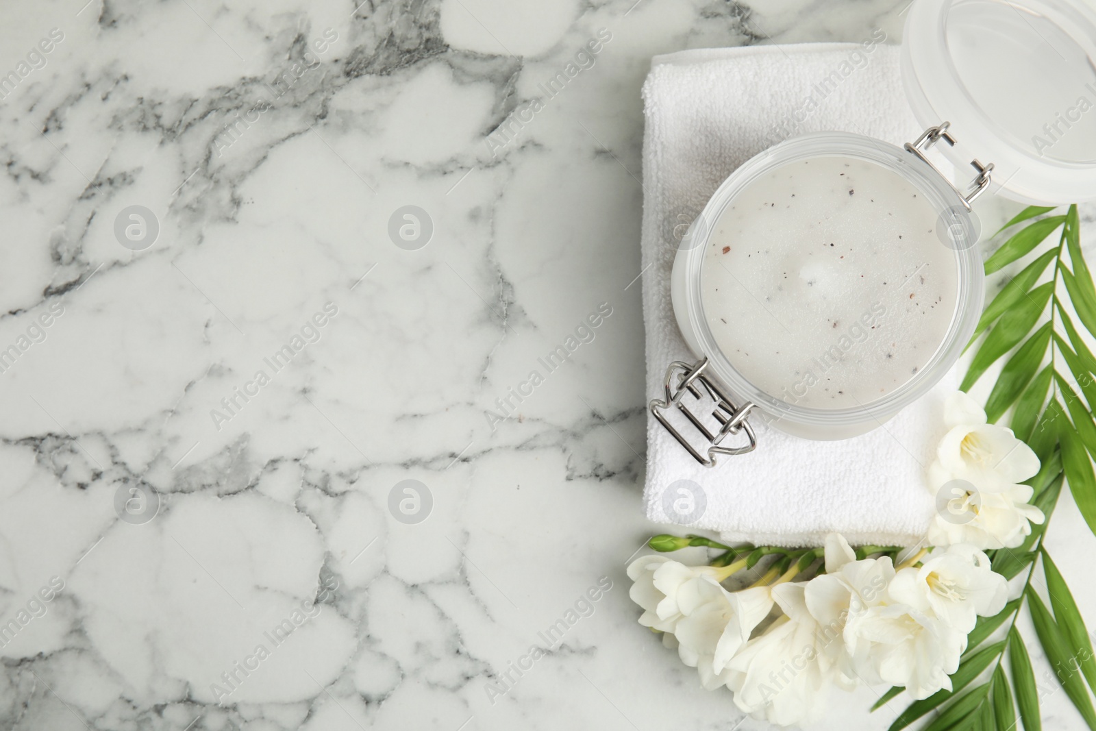 Photo of Jar of salt scrub, freesia flowers and towel on white marble table. Space for text