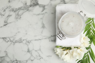 Jar of salt scrub, freesia flowers and towel on white marble table. Space for text