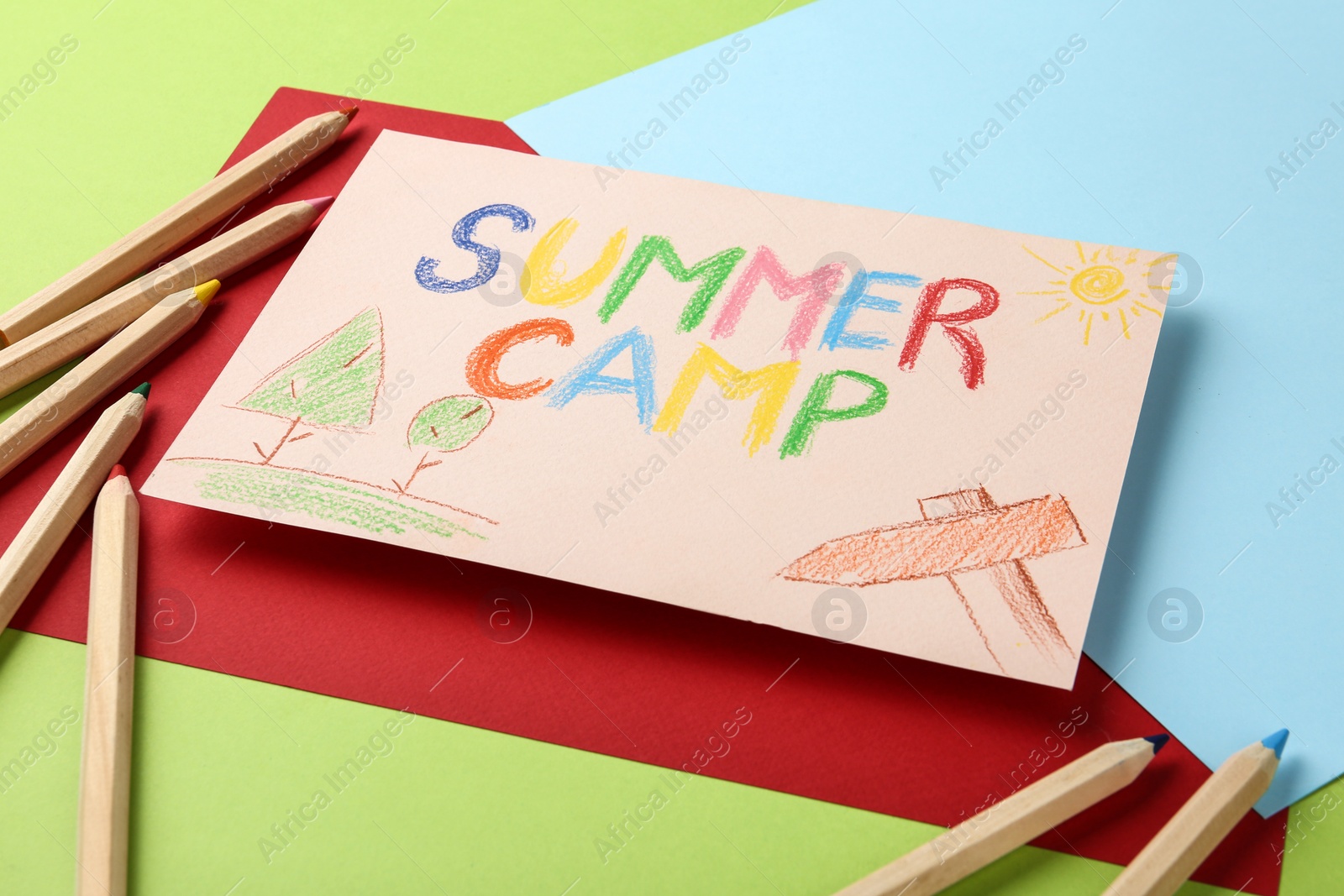 Photo of Paper with written text SUMMER CAMP, drawings and different pencils on color background, closeup