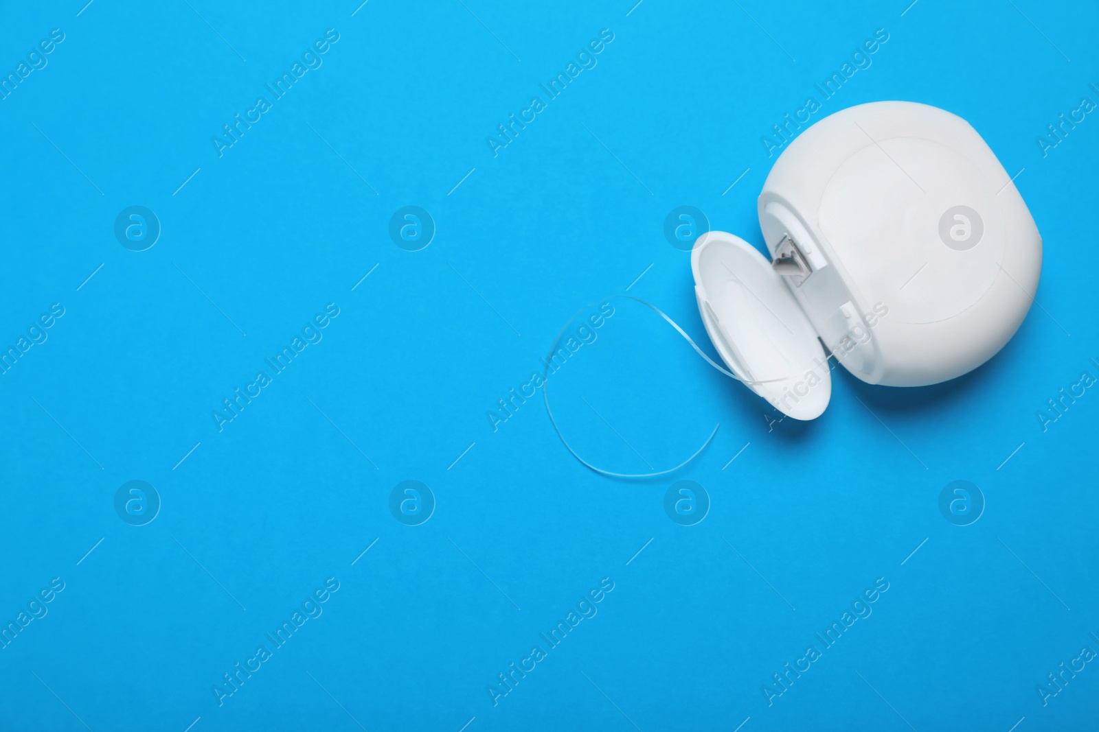 Photo of Container with dental floss on light blue background, top view. Space for text