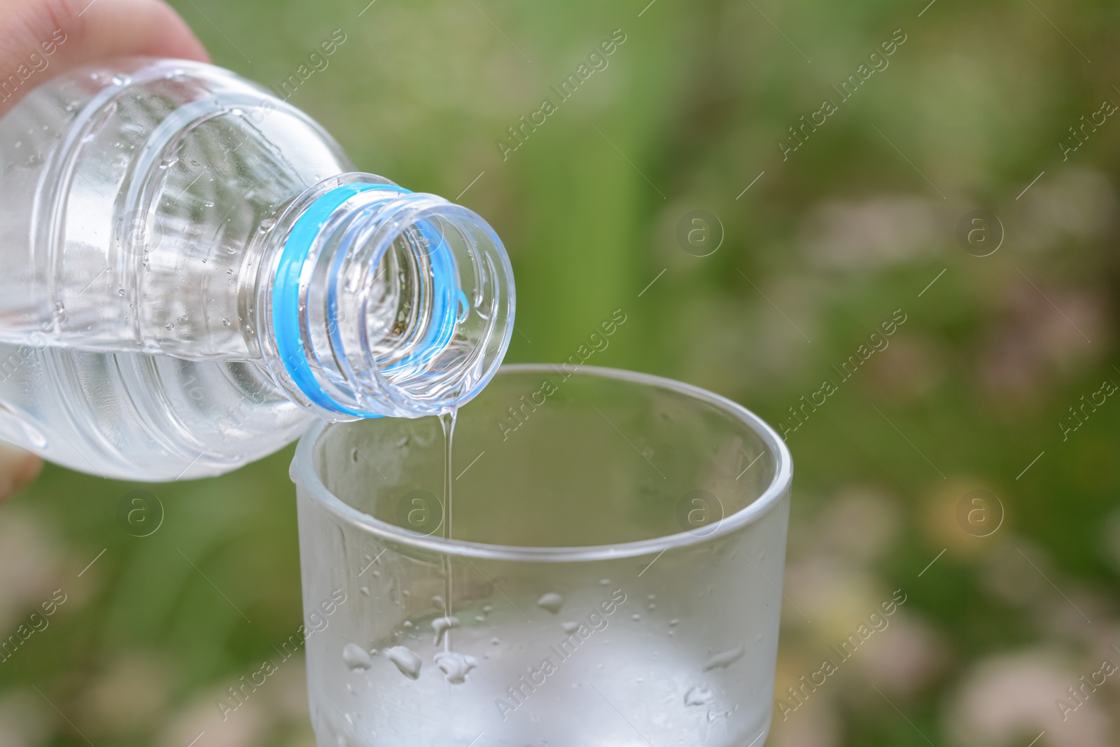 Photo of Woman pouring water from bottle into glass outdoors, closeup