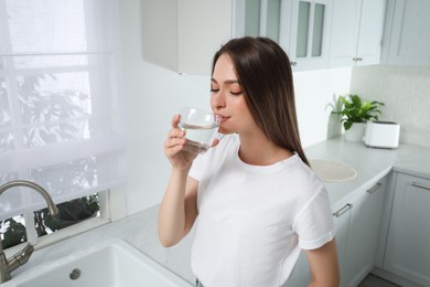 Photo of Woman drinking tap water from glass in kitchen