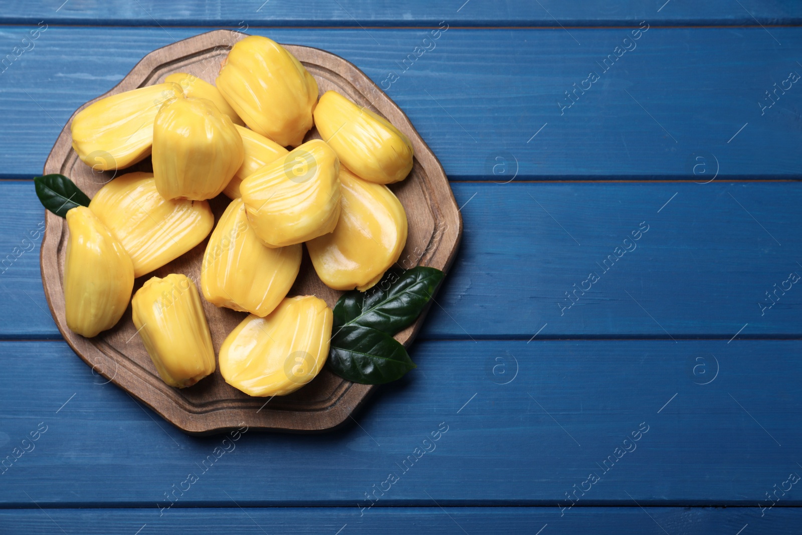 Photo of Delicious exotic jackfruit bulbs on blue wooden table, top view. Space for text