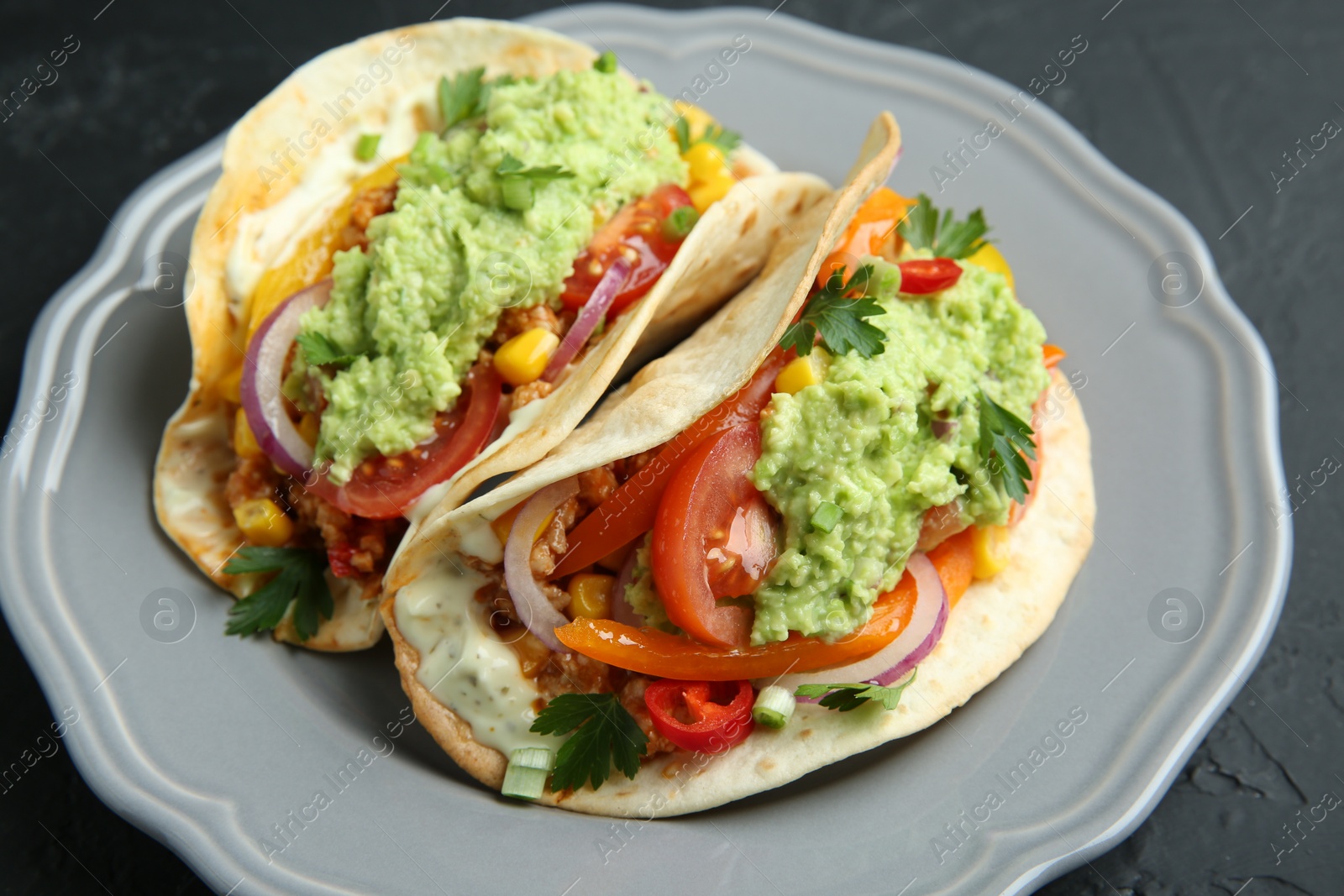 Photo of Delicious tacos with guacamole, meat and vegetables on black table, closeup