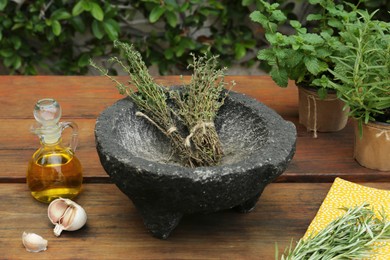 Photo of Mortar, different herbs, garlic and oil on wooden table