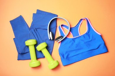 Photo of Stylish sportswear, dumbbells and headphones on orange background, flat lay