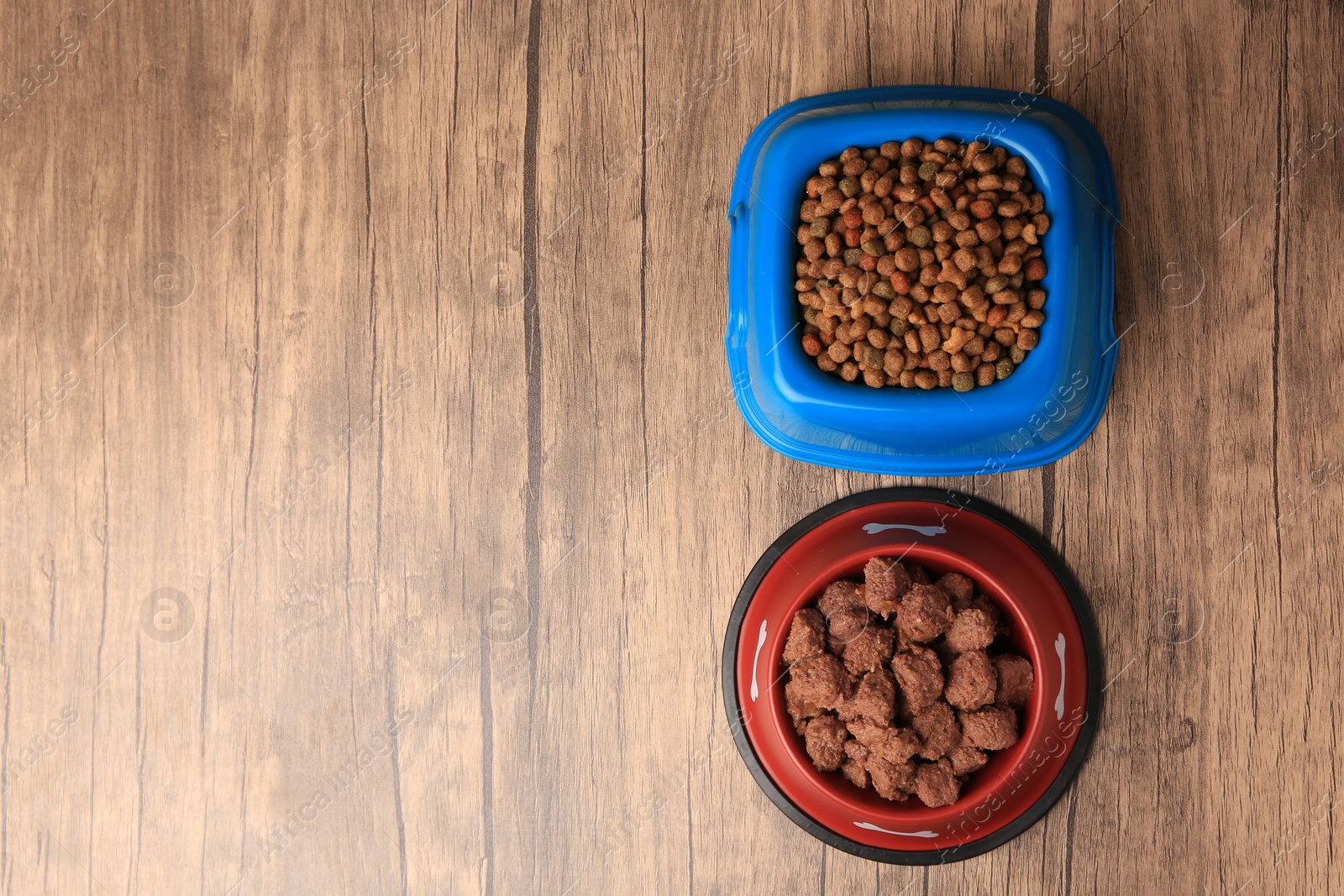 Photo of Dry and wet pet food in feeding bowls on wooden background, flat lay. Space for text