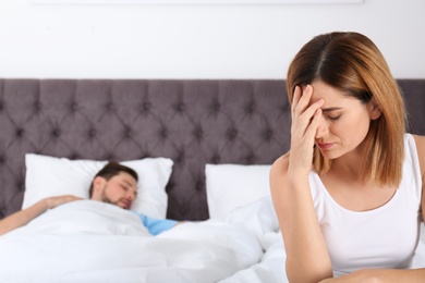 Upset woman sitting on bed near her sleeping husband at home. Relationship problems