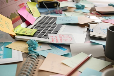 Laptop, notes and office stationery in mess on desk. Overwhelmed with work