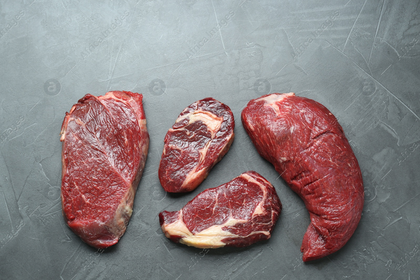 Photo of Pieces of raw beef meat on grey table, flat lay. Space for text