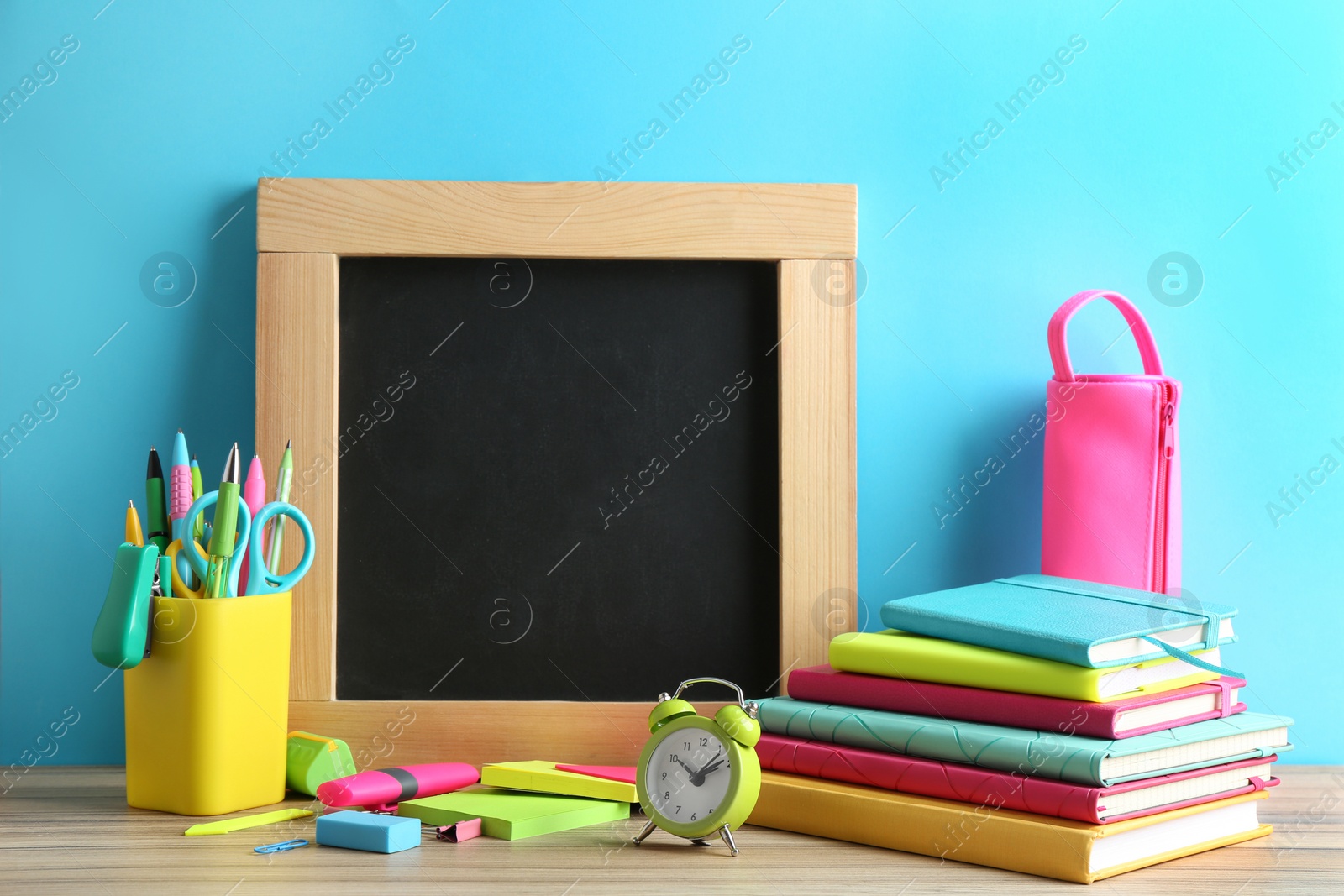 Photo of Different school stationery and small blank chalkboard on table near light blue wall. Space for text